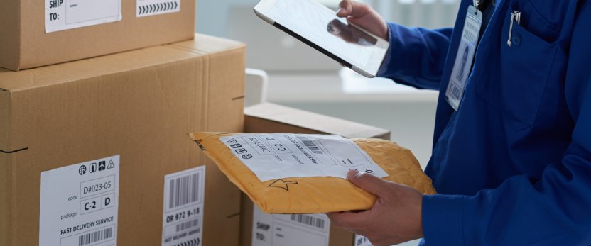 Boxes are stacked on a table while a person checks shipping info on a tablet. 